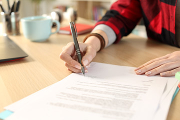 Student hands signing contract sitting at home