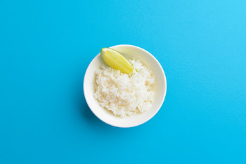 White rice with a piece of lime served in a small white bowl. Isolated on bright blue background.