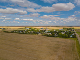 Drone footage aerial of village in the middle of fields nowhere in Canada Saskatchewan between roads and fields during sunset with blue sky and clouds 
