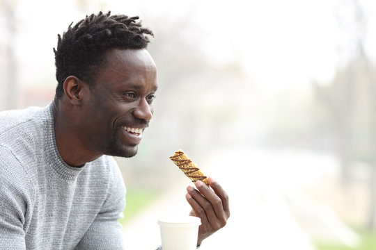 Happy black man having coffee and snack bar in a park