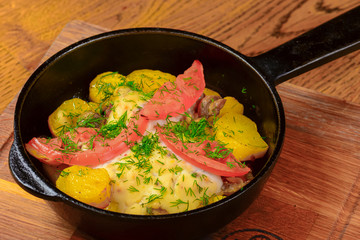 Roasted potato with tomatoes and dill in a frying pan on wooden table. Tasty delicious dinner.