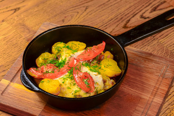 Roasted potato with tomatoes and dill in a frying pan on wooden table. Tasty delicious dinner.