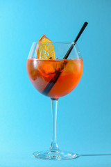 A glass of fruit liqueur in wine glass with a piece of lemon and black plastic straw isolated on pastel blue background.