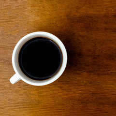 Coffee cup on wooden kitchen table. Top view with morning sunlight