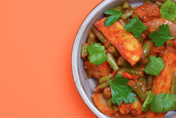 Stew of chicken meat with vegetables served in a bowl over bright orange background. Design banner with copy space.
