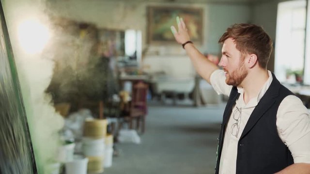 Focused stylish artist paints a painting by throwing dry paint on the canvas