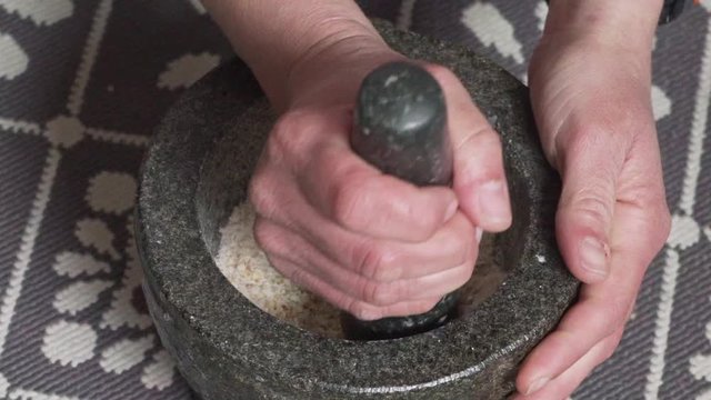 Footage of woman pulverising Chios Mastic and Mahaleb in granite mortar, slow motion medium shot