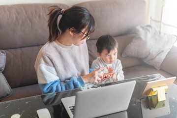 Young woman working from home. Home workplace with kids. Disinfect kid hands with sanitizer alcoholic gel. Mother working with laptop in living room. Home office during virus quarantine