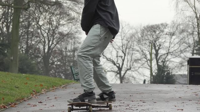 Closed frame in slowmotion of a skateboarder doing tricks through the streets of Manchester in winter, the street is full of leaves and ice