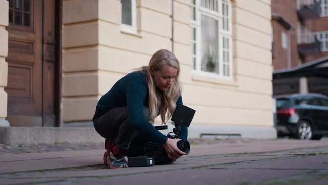 Female filmmaker checks lens and puts lens and battery on cinema camera