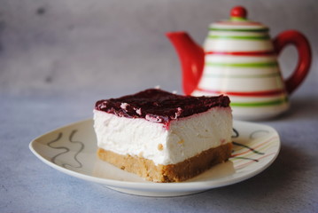 Homemade Raspberry Cheesecake Slice served in a little white plate, teapot in the background.