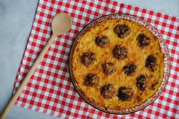 Meatballs and Mashed Potatoes Casserole in a glass pan, served on a plaid kitchen napkin. Top view.