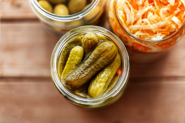 Various pickled snacks in cans, cucumber pickles, salted cabbage and olives. On a wooden table. View from above