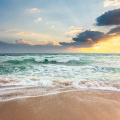 storm on the sandy beach at sunset. dramatic ocean scenery with cloudy sky. rough water and crashing waves in evening light