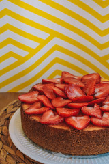 Homemade cheesecake with fresh strawberries is photographed on a bright yellow background with a plant branch