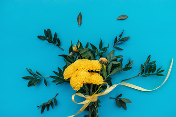 Bouquet of yellow chrysanthemums and pistacia leaves, tied with a yellow ribbon on a blue background.Festive greeting card for Valentine's Day, Woman's Day, Mother's Day, Easter,8 March, birthday