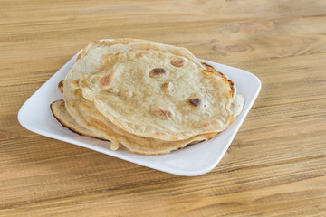 Pita bread in white plate on light wooden background.