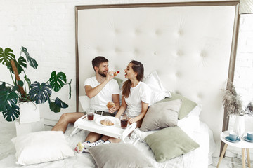 Cute couple in a bedroom. Lady in a white t-shirt. Man brought breakfast to bed.