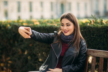 Stylish beautiful lady in a black leather jacket with a black bag and burgundy blouse. Attractive young woman use phone