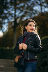 Fototapeta na wymiar Stylish beautiful lady in a black leather jacket with a black bag and burgundy blouse. Attractive young woman smile