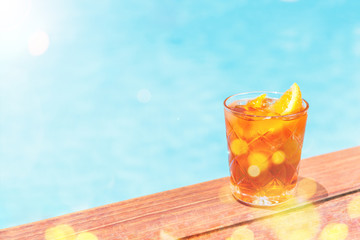 Negroni cocktail near a pool at resort bar or suite patio. Luxury resort, vacation, holiday, getaway, summer time, room service concept. Horizontal with place for text with festive bokeh and sunlight