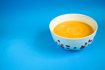 Orange soup puree of pumpkin, potatoes, carrots and cream in a white plate on a blue background.  Dinner and supper