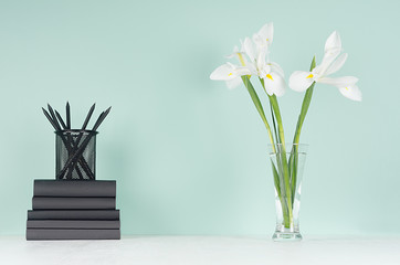 Obraz na płótnie Canvas Modern elegant home workplace with black stationery, books, fresh spring white flowers in transparent glass vase green mint menthe interior on white wood table.
