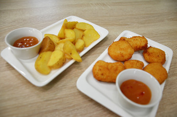 chicken nuggets and fried potatoes on a white plate on a table in a cafe or restaurant