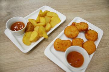 chicken nuggets and fried potatoes on a white plate on a table in a cafe or restaurant