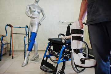 Prosthetist man with prosthetic leg in laboratory against wheelchair.