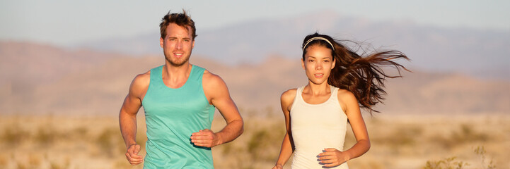 Fit healthy runners couple running on outdoor trail training athletes banner panoramic. Beautiful young Asian woman and Caucasian man exercising cardio.