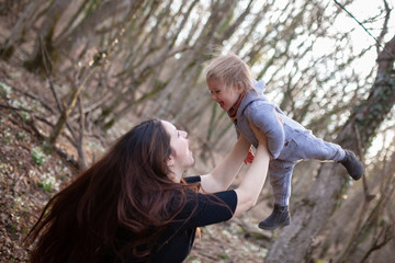 Happy pregnant mother throws her baby up, mom and daughter walk in the spring forest
