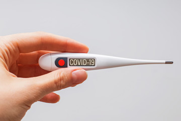 Hand holds clinical thermometer with covid-19 text on the screen d