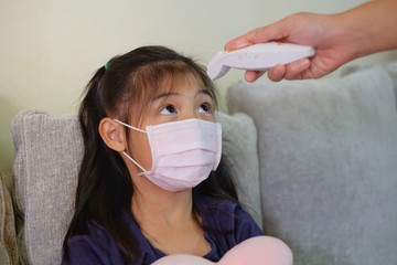 A mother periodically monitoring her daughter's temperature using an infrared thermometer at her...