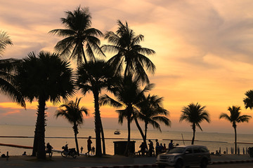 Silhouette of tourists and coconut trees by the sea at sunset.