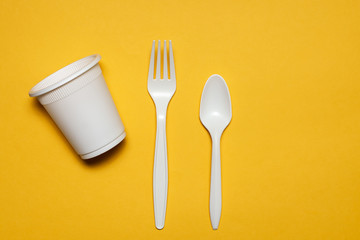 disposable glass, spoon and fork of corn starch on a yellow background. biodegradable eco friendly picnic tableware. isolate. replacement of plastic with modern biomaterials.