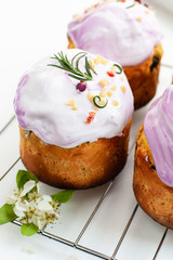 Beautiful Easter cakes with white and pale pink icing decorated with candied fruit, dried roses and sprigs of herbs on baking rack. Traditional festive pastries of christians close up. Selective focus
