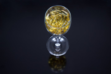 Yellow omega-3 capsules in a glass on a glossy black background with a reflection. The concept of healthy eating.