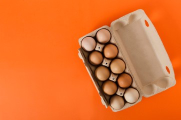 Top view of raw eggs in the carton box on the orange background.Empty space