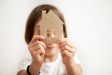 Little girl holding paper house in front of her face. Protect your home concept