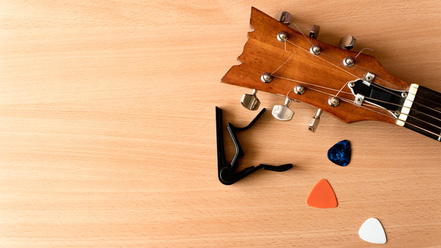 Acoustic guitar, capo and picks lie on a wooden background. Music concept with copy space.