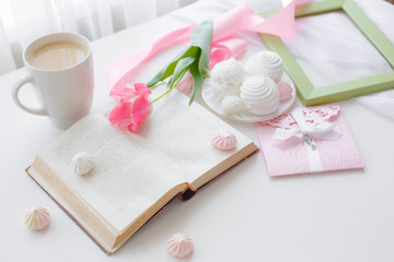 postcard good morning. Still life : a Cup of tea, a bouquet of pink tulips, a marshmallow book on a light background near the window.