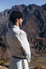 noise effect, selective focus: stylish Georgian man dressed in white national men's suit. Portrait of Georgian groom during wedding on Caucasus mountains