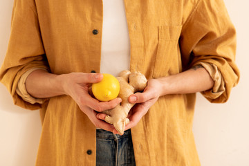 Woman in a beige jacket holding a lemon with and a ginger root two hands