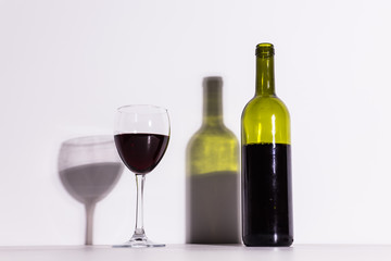 A glass of wine and a bottle casts a long shadow from the evening sun.