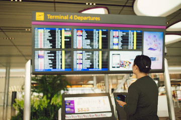 Passenger traveling at the flight information board in airport terminal waiting hall area checking...