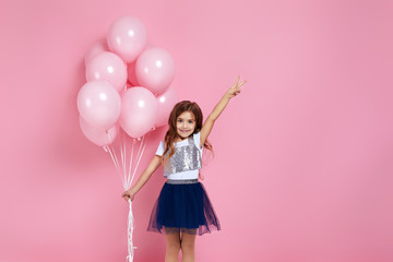 Obraz na płótnie Canvas Smiling adorable little child girl with pastel pink air balloons showing peace gesture isolated over pink background. Beautiful happy kid on a birthday party. space for text