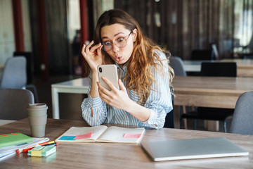 Image of shocked charming woman using cellphone and expressing surprise