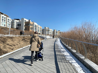 Vladivostok, Russia, March, 13,2020.  Young woman with a stroller walking along the promenade in Patroclus (Patrokl) bay in early spring. Vladivostok, Russia