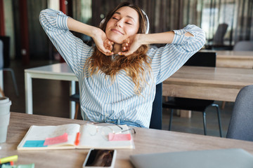 Image of relaxed young woman using headphones and stretching her body